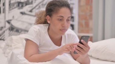 Afrika kökenli Amerikalı Kadın, karnının üstünde yatarken akıllı telefon kullanıyor.