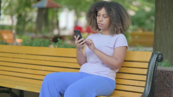 坐在室外长椅上使用智能手机的非洲青年妇女 — 图库视频影像