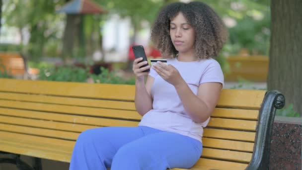 ベンチに座っている間に電話でオンライン決済の失敗によって動揺若いアフリカの女性 — ストック動画