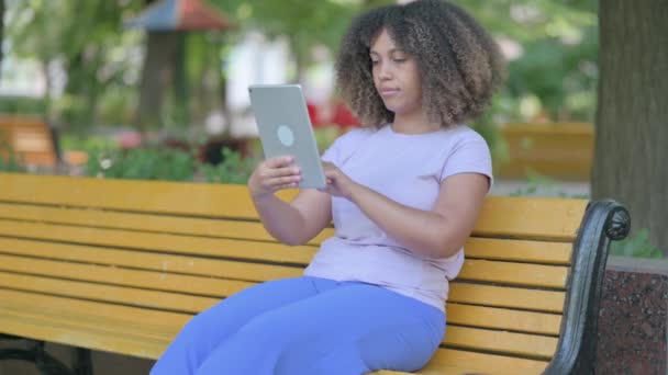 年轻的非洲妇女坐在户外的长椅上庆祝在桌面上的成功 — 图库视频影像