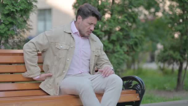 腰を痛めながらベンチに腰掛けている中年男性 — ストック動画