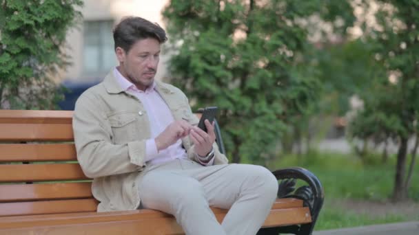 Homme Moyen Âge Célébrant Succès Sur Smartphone Tout Étant Assis — Video
