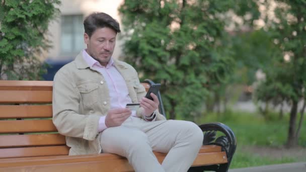 ベンチで屋外に座っている間に電話で中年男性のショッピングオンライン — ストック動画