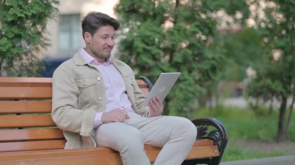 中年人坐在户外的长椅上 一边坐在桌子上一边做视频聊天 — 图库视频影像