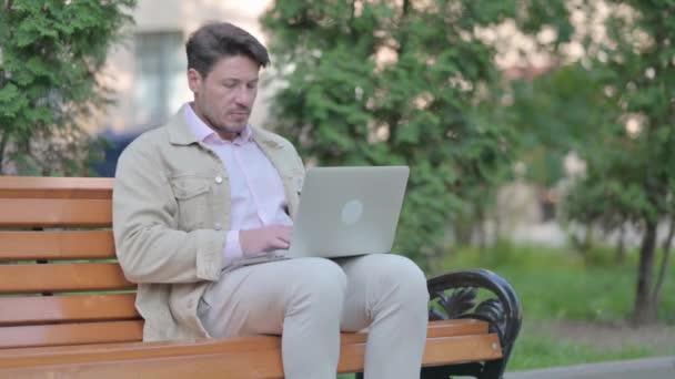 ベンチに座っている間にラップトップを閉めた後に出る中年の男 — ストック動画