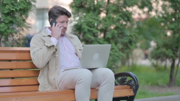 Mężczyzna Średnim Wieku Rozmawia Przez Telefon Podczas Siedzenia Zewnątrz Ławce — Wideo stockowe