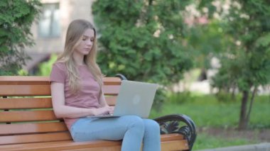 Genç bir kadın bankta otururken öksürüyor ve dizüstü bilgisayar kullanıyor.