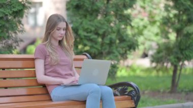 Dizüstü bilgisayarını kapattıktan sonra bankta oturan genç bir kadın.