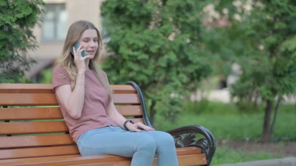 Bankta Otururken Telefonda Konuşan Heyecanlı Genç Bir Kadın — Stok video