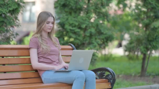 若い女性はノートパソコンの屋外で作業しながらカメラで微笑む — ストック動画