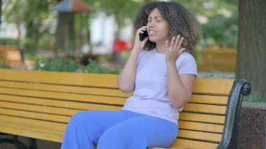 Bankta otururken telefonda tartışan Afrikalı genç bir kadın.
