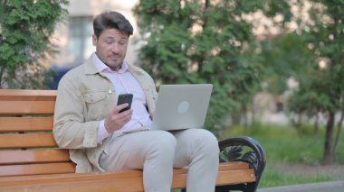 Laptop ve Smartphone 'da çalışan orta yaşlı bir adam.