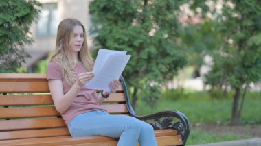 Bir bankta otururken Genç Kadın Sözleşmeyi okurken Üzülüyor