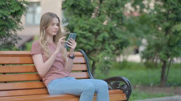 ベンチに座っている間にスマートフォンを使う若い女性 — ストック写真