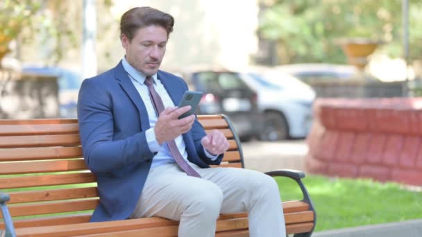 商人坐在户外的长椅上使用智能手机 — 图库视频影像