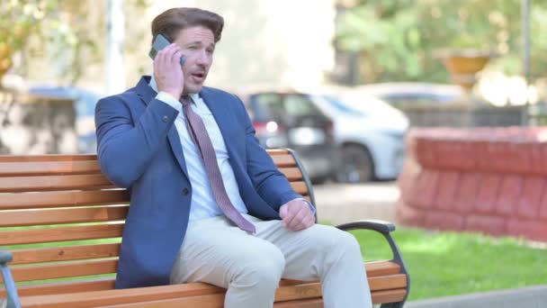 Biznesmen Rozmawianie Przez Telefon Podczas Siedzenia Zewnątrz Ławce — Wideo stockowe