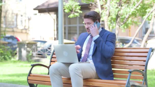 Μεσήλικας Επιχειρηματίας Μιλώντας Στο Τηλέφωνο Και Χρησιμοποιώντας Laptop Outdoor — Αρχείο Βίντεο