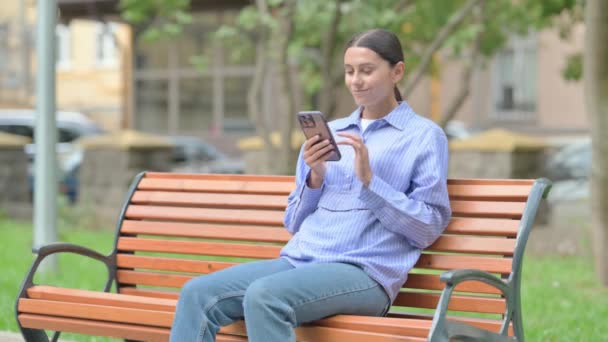 Mujer Hispana Usando Smartphone Mientras Está Sentada Aire Libre Banco — Vídeo de stock