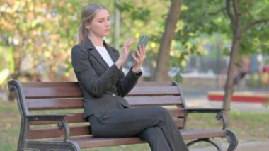 İş kadını Bench 'te otururken telefonu kullanıyor.