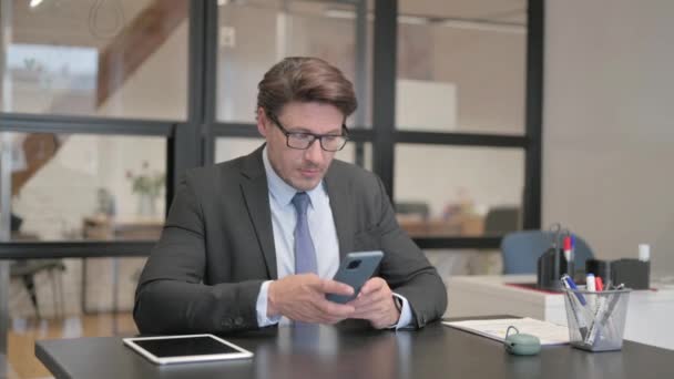 Επιχειρηματίας Που Χρησιμοποιεί Τηλέφωνο Ενώ Κάθεται Στο Γραφείο — Αρχείο Βίντεο