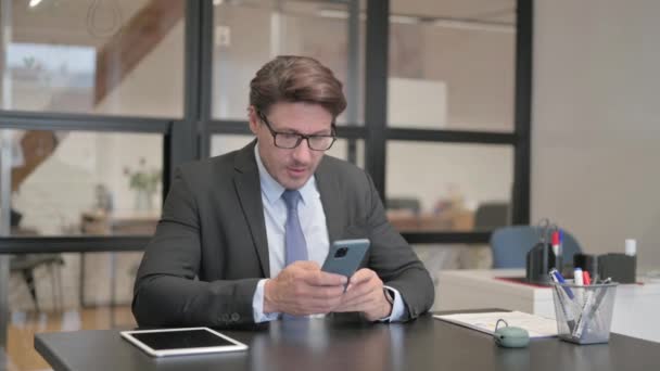 商界人士一边坐在办公室一边一边在电话上庆祝网上成功 — 图库视频影像