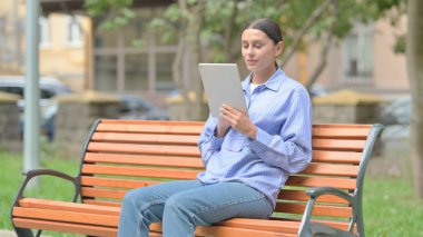 Bir bankta otururken tablet kullanan İspanyol kadın.