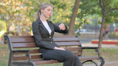 Bekleyen İş Kadını Bench 'te otururken Bilek İzleme Saati