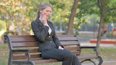 İş kadını Bench 'te otururken diş ağrısı çekiyor.