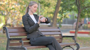 İş kadını Bench 'te otururken Smart Watch kullanıyor.