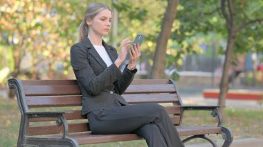 İş kadını Bench 'te otururken telefonu kullanıyor.