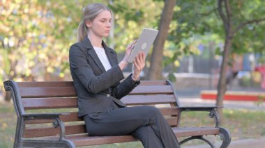 Bir bankta otururken Tablet kullanan bir iş kadını