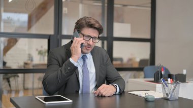 Ofiste bir bankta oturan işadamı telefonda konuşuyor.