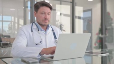 Bilgisayarda çalışırken kameraya bakan orta yaşlı doktor