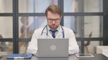 Hastanede dizüstü bilgisayarda çalışırken kameraya bakan doktor.