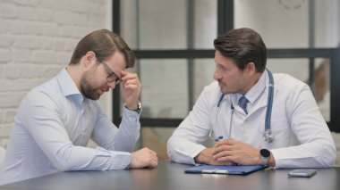 Baş ağrısı olan bir adam orta yaşlı bir doktora danışmanlık yapıyor.