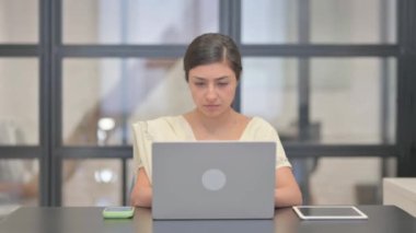 Bilgisayarda çalışırken kameraya gülümseyen genç Hintli kadın.