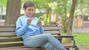 Açık havada oturan Hintli Kadın İnternet üzerinden kredi kartı ve telefonla alışveriş yapıyor.