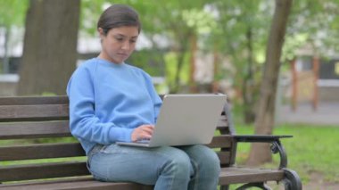 Açık havada oturan Hintli kadın dizüstü bilgisayar kullanırken kameraya bakıyor