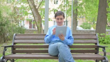 Bankta otururken tablet kullanan Hintli kadın.