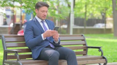 Bankta otururken akıllı telefon kullanan bir işadamı.