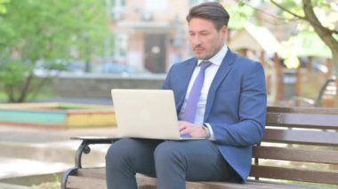 İş adamı Bench 'te otururken dizüstü bilgisayarda çalışıyor.