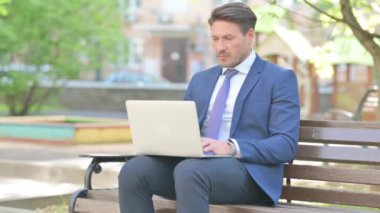 Migreni olan bir iş adamı Bench 'te otururken dizüstü bilgisayar kullanıyor.