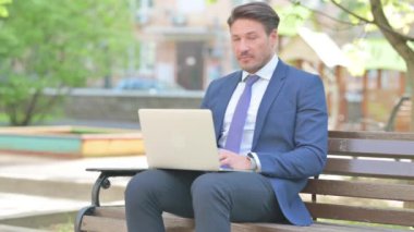 Bench 'te otururken dizüstü bilgisayar kullanan İşadamından Başparmak Yukarı