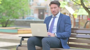 Bankta dizüstü bilgisayar kullanırken kameraya bakan iş adamı şok oldu.