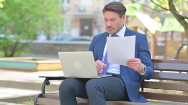 Bench 'te otururken Belgeler ve Laptop üzerinde çalışan İşadamı