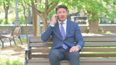 Orta yaşlı işadamı dışarıda telefonla konuşuyor.
