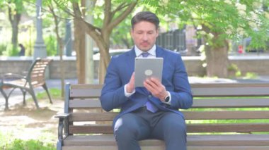 Orta yaşlı işadamı açık havada otururken tablet kullanıyor