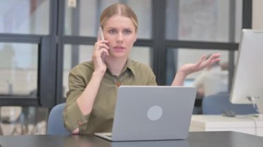 Kızgın İş Kadını Dizüstü bilgisayarla çalışırken telefonla konuşuyor