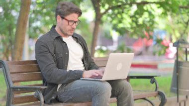 Düşünceli Orta Çağ Adamı Bench 'te otururken laptopta kitap okuyor.