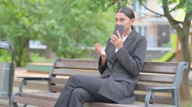 Kızgın İspanyol iş kadını dışarıda otururken telefonda konuşuyor.